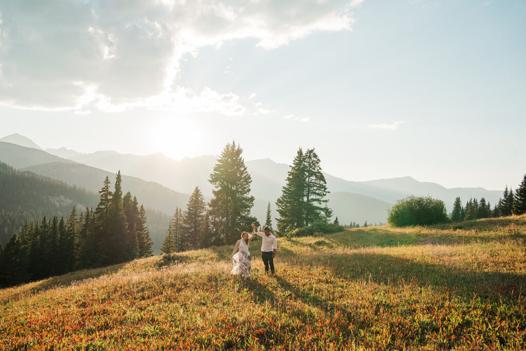 A couple dances in a field at sunset with mountain in the background along a mountain pass near Breckenridge, Colorado