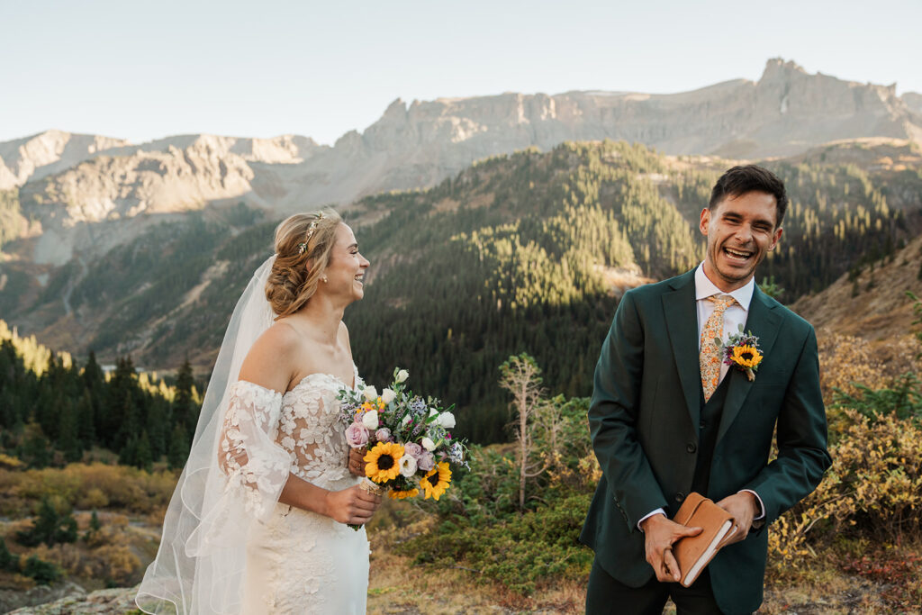 A couple laughs towards the camera surrounded by mountains in Ouray, Colorado