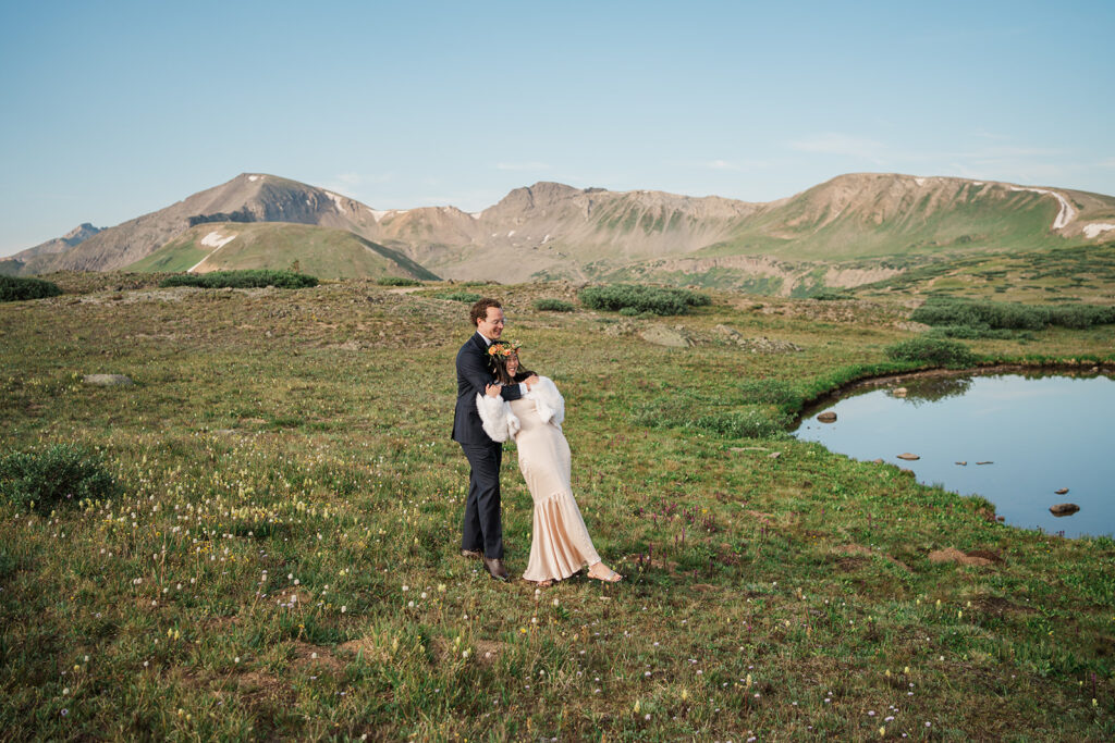 A couple embraces in a meadow of wildflowers near an alpine lake in Aspen, Colorado